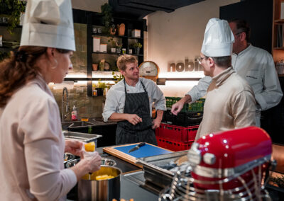 Mehrere Personen kochen gemeinschaftlich in einem Kochstudio. Dabei werden Kartoffeln geschält und Gespräche mit dem Koch geführt.